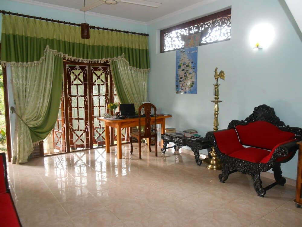 A serene living room with tiled floors, green curtains, a red upholstered bench, and a map of Sri Lanka on the wall offers a cozy space for travelers seeking relaxation and cultural ambiance.