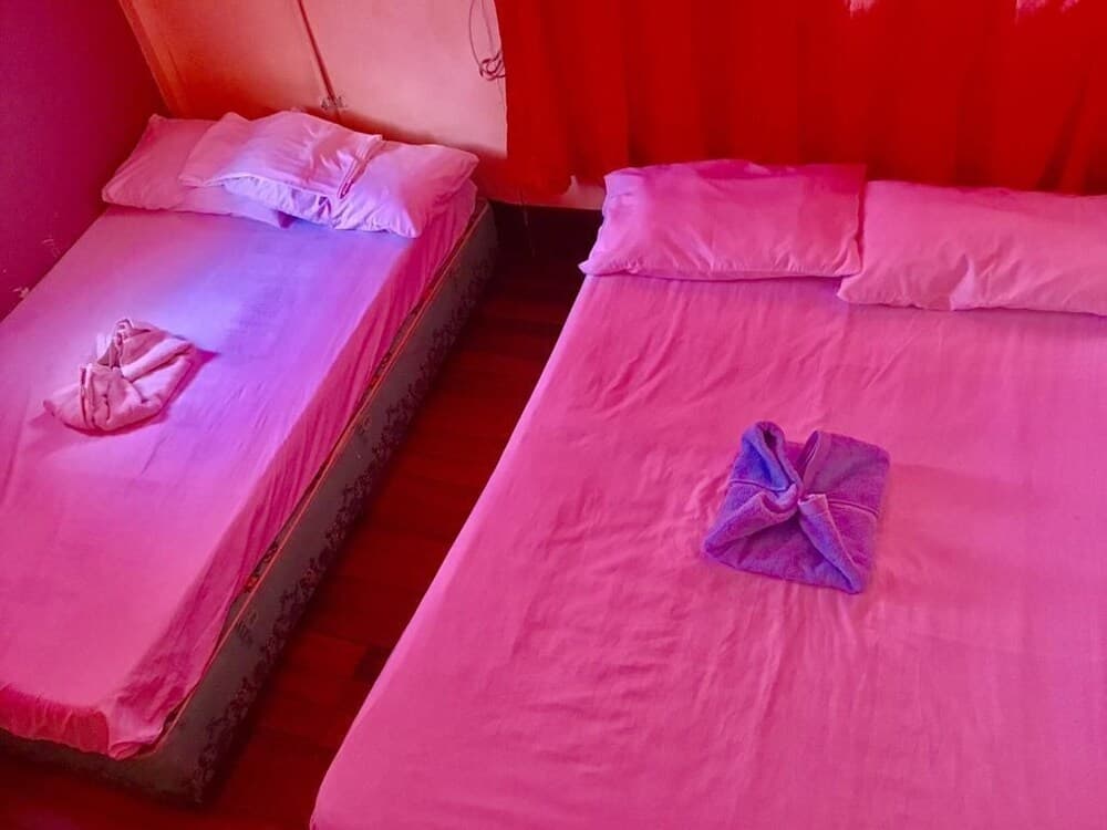 A cozy budget-friendly guesthouse room features two single beds with pink linens, folded towels, and red curtains, creating a warm and inviting atmosphere ideal for solo travelers or couples seeking affordable accommodations.