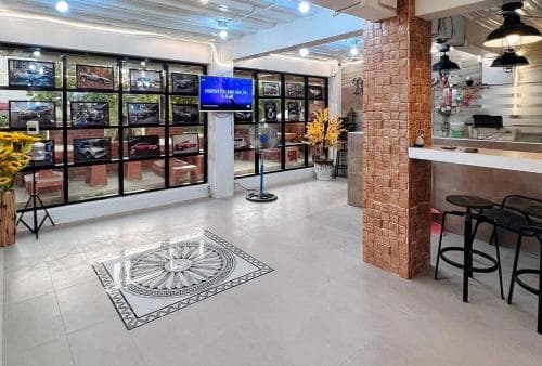 A modern indoor space features a sleek tiled floor, vibrant yellow flowers, a brick column, and glass display cases filled with framed photos, creating an inviting atmosphere ideal for a casual meet-up or small exhibition venue.