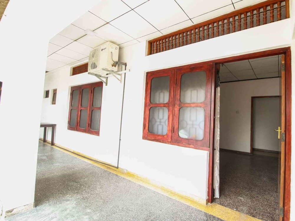 A serene indoor corridor with polished floors, wooden-framed doors and windows, and an air conditioning unit creates a calm atmosphere ideal for travelers seeking a quiet accommodation space.