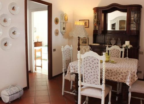 A cozy dining area with floral tablecloth-covered chairs, a wooden cabinet, decorative plates on the wall, and warm lighting creates an inviting atmosphere ideal for travelers seeking a charming and homely accommodation experience.