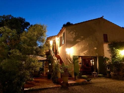 A cozy evening scene at a rustic villa illuminated by warm lights, surrounded by lush greenery, ideal for travelers seeking a serene countryside retreat.