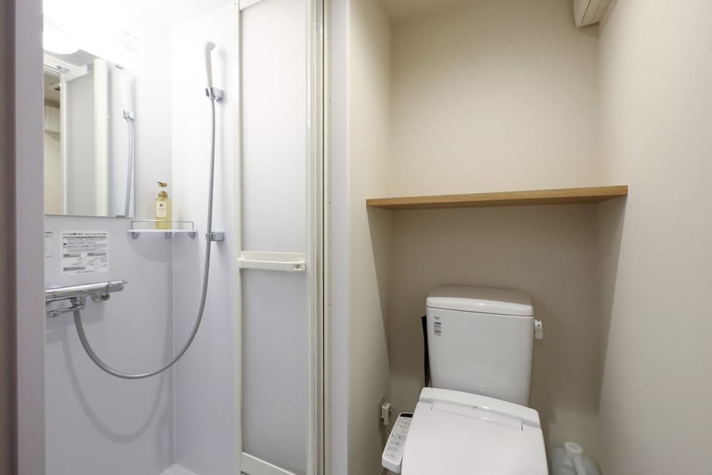 A compact, modern bathroom features a sleek shower area with a handheld faucet, a wall-mounted mirror, and a high-tech toilet with a control panel, ideal for travelers seeking efficient and clean accommodations.