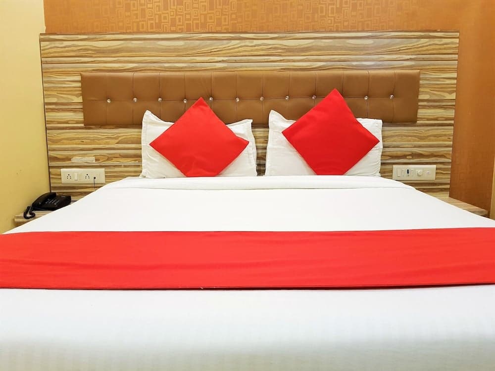 A cozy hotel room features a neatly made bed with white linens, vibrant red accents, and a wooden headboard, ideal for travelers seeking comfort and style.