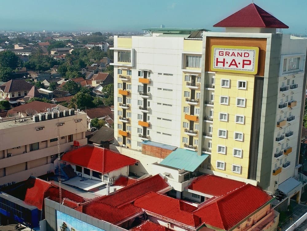 A vibrant urban scene featuring the "Grand H·A·P" hotel with its distinctive yellow facade and red-roofed structures, set against a backdrop of residential rooftops, ideal for travelers seeking a mix of modern amenities and local charm.