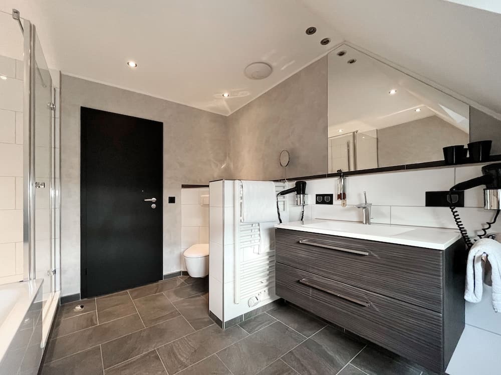 A modern bathroom with sleek gray tiles, a spacious vanity, a walk-in shower, and a cozy attic vibe offers a serene retreat for travelers seeking comfort and style.