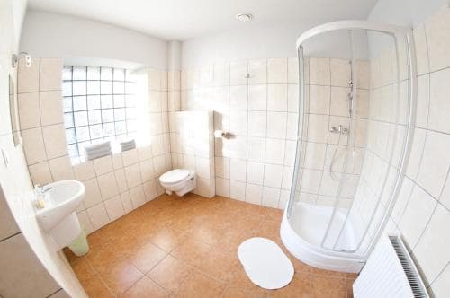 A clean, well-lit bathroom with beige tiles, a shower enclosure, toilet, sink, and frosted window offers a functional space ideal for travelers seeking comfort in accommodations.