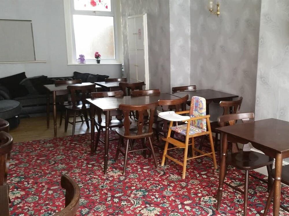 A cozy café with wooden tables and chairs, a colorful patterned rug, and a high chair, offers a welcoming atmosphere for families and travelers seeking a comfortable spot to relax and dine.