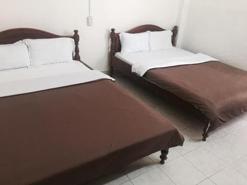 A cozy budget hotel room features two neatly made beds with brown blankets against a minimalist white backdrop, ideal for travelers seeking simple accommodations.
