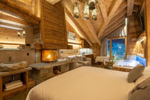 A cozy, rustic cabin bedroom with wooden beams, a warm fireplace, and a scenic view through large windows, perfect for a romantic getaway or winter retreat.