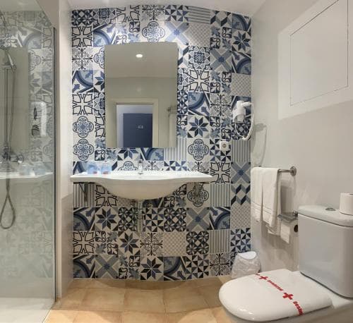 A stylish bathroom features vibrant blue and white patterned tiles around a modern sink, creating a chic and inviting atmosphere ideal for travelers seeking comfort and design in their accommodations.