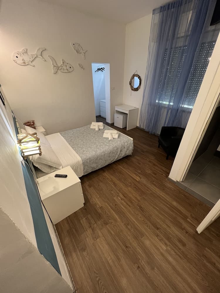 A cozy bedroom with wooden flooring, white furnishings, fish wall art, and blue curtains creates a serene atmosphere ideal for travelers seeking a comfortable and stylish accommodation.