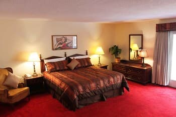 A cozy hotel room features a plush bed with patterned bedding, warm lighting from bedside lamps, and red carpeting, creating an inviting atmosphere ideal for travelers seeking comfort and relaxation.