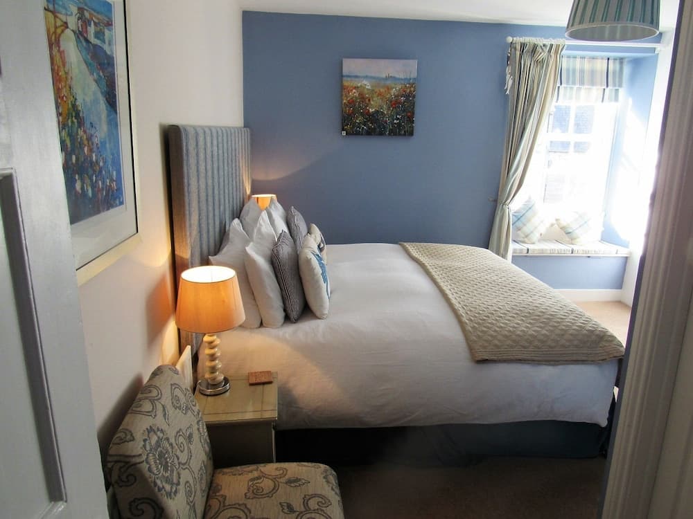 A cozy bedroom with soft blue walls, floral artwork, and a sunlit window creates a serene retreat, ideal for travelers seeking relaxation and comfort.