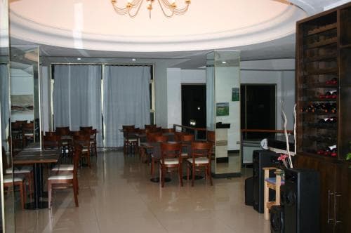 A cozy hotel lounge features wooden tables and chairs under soft lighting, with a wine rack adding charm, ideal for travelers seeking a quiet spot to unwind or dine.