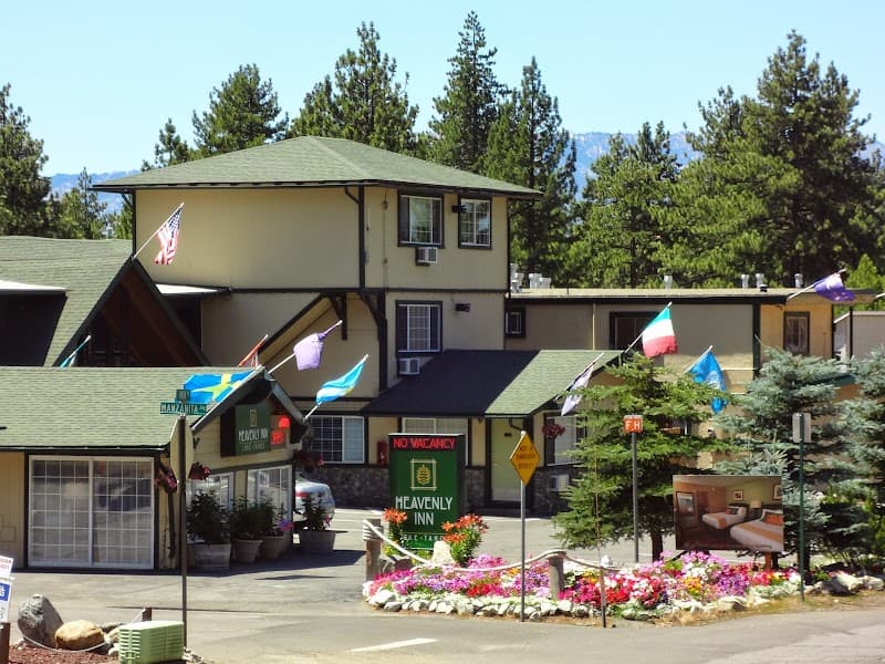 The inviting Heavenly Inn in South Lake Tahoe, surrounded by lush pine trees and vibrant flower beds, offers a cozy retreat with its charming architecture and welcoming atmosphere, perfect for travelers seeking relaxation in a picturesque mountain setting.