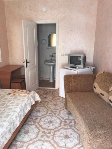A cozy budget-friendly hotel room features a patterned tile floor, a small bed, a sofa, a desk, and an attached bathroom, ideal for travelers seeking simple accommodations.