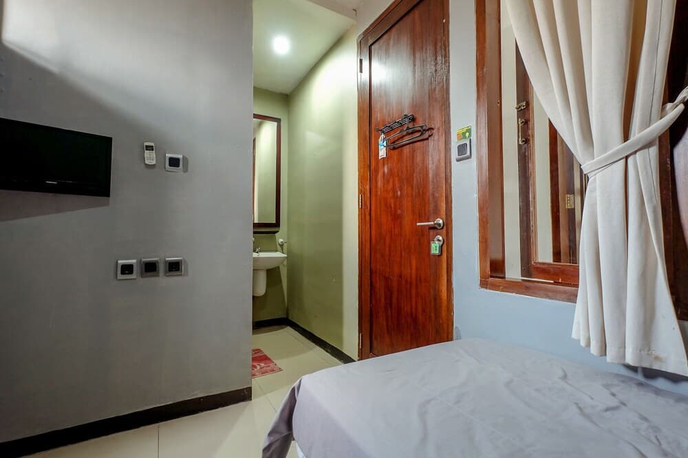 A cozy budget hotel room features a neatly made bed, wooden door, wall-mounted TV, and an en-suite bathroom visible through an open doorway, ideal for travelers seeking simple accommodations.