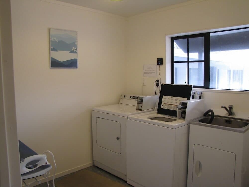 A cozy laundry room with white appliances, a sink, an ironing board, and a serene wall art piece offers travelers a convenient spot to refresh their clothes during their stay.