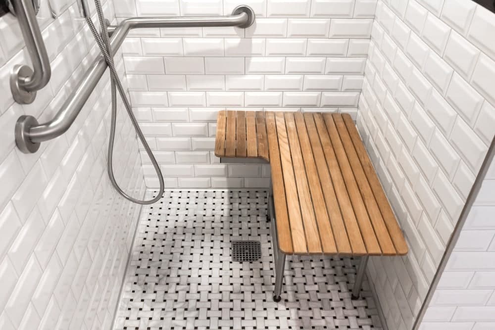 A modern, accessible shower space features white subway tiles, a wooden bench, and stainless steel fixtures, ideal for travelers seeking comfort and convenience in accommodations.