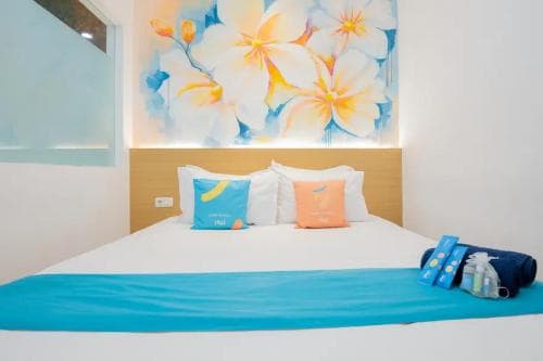 A cozy hotel room features a neatly made bed adorned with colorful pillows and a vibrant floral mural above, creating a cheerful and inviting atmosphere ideal for travelers seeking comfort and relaxation.