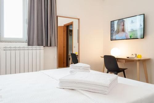 A cozy hotel room features a neatly made bed with folded towels, a desk with modern decor, and a TV displaying a serene scene, ideal for travelers seeking comfort and relaxation.