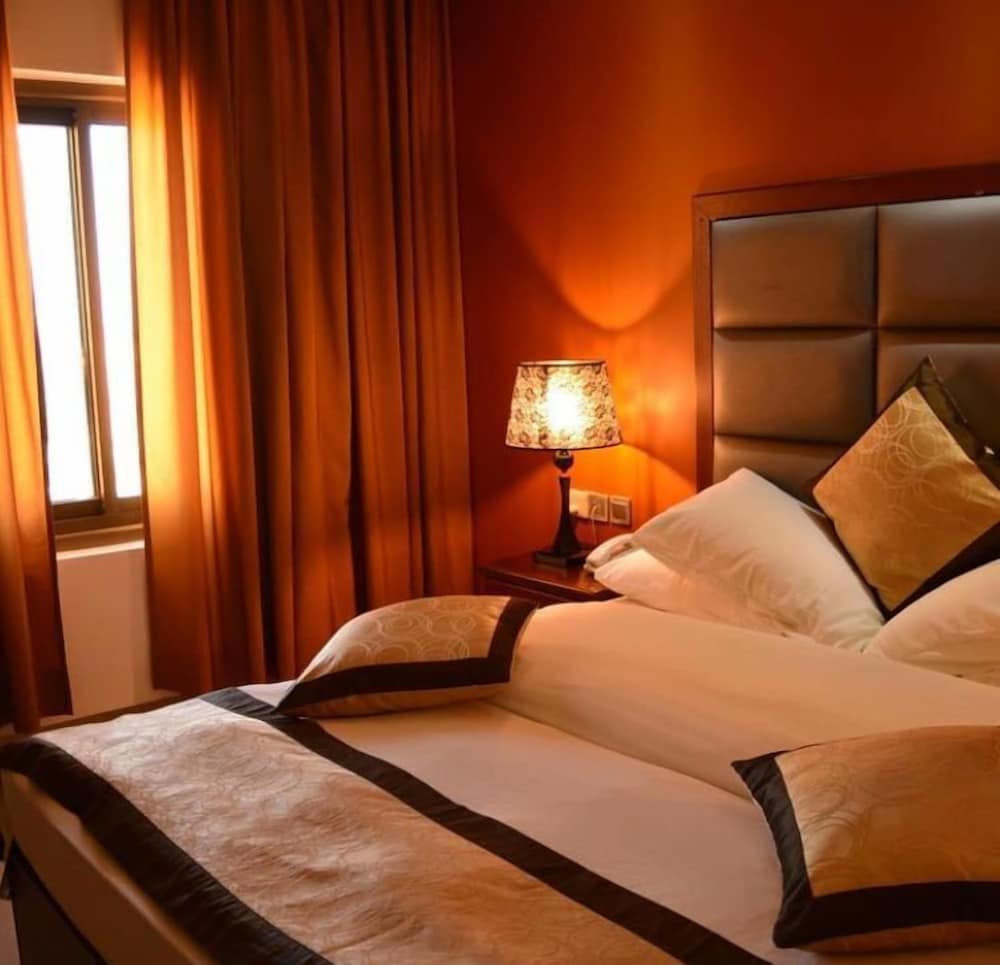A cozy hotel bedroom with warm orange walls, plush bedding, and a glowing bedside lamp creates an inviting atmosphere ideal for travelers seeking comfort and relaxation.