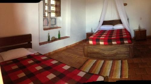 A cozy rustic bedroom with wooden beds adorned in red plaid bedding, a striped rug, and a window ledge with bottles, ideal for a serene getaway experience.