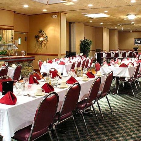 A warmly lit banquet hall set up for an event features tables draped in white linens with red napkins, creating an inviting atmosphere ideal for conferences or celebrations.