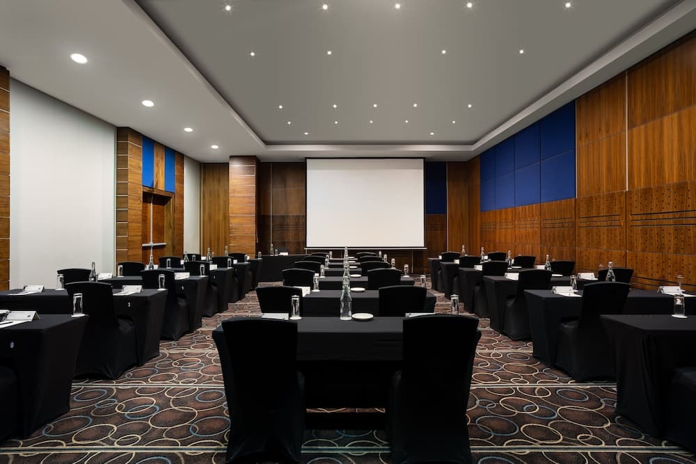 A modern conference room with sleek wooden walls, blue accents, and rows of black tables set for a professional event, ideal for business travelers seeking a sophisticated meeting venue.