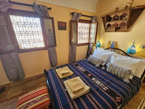 A cozy, warmly lit bedroom with patterned textiles, decorative windows, and ornate shelves creates an inviting atmosphere ideal for travelers seeking a culturally rich accommodation experience.