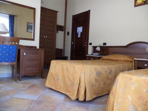 A cozy hotel room with tiled floors, wooden furniture, and floral bedspreads offers a comfortable stay for travelers seeking a warm and inviting atmosphere.