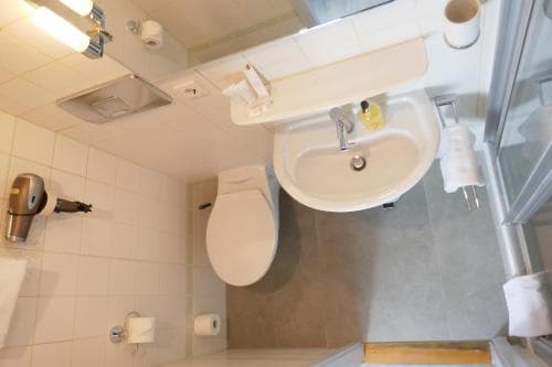 A compact hotel bathroom features a sink, toilet, and shower area with white tiles, creating a clean and functional space ideal for travelers seeking efficient accommodations.