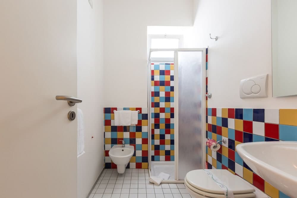 A vibrant bathroom with colorful mosaic tiles, white fixtures, and natural light from a skylight creates a cheerful and inviting atmosphere ideal for travelers seeking a cozy accommodation.