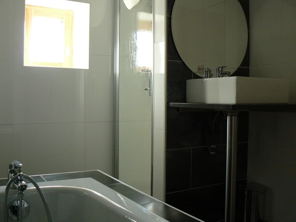 A modern bathroom features a sleek bathtub, glass shower enclosure, and a minimalist sink under a round mirror, ideal for travelers seeking clean and contemporary accommodations.