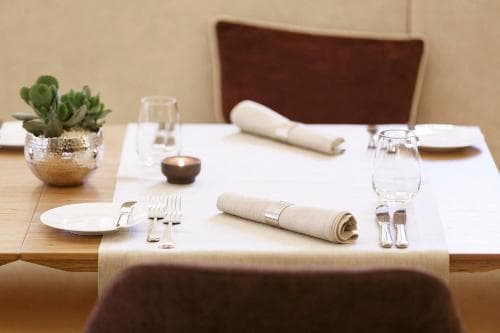 A cozy restaurant table set with elegant white linens, neatly rolled napkins, and a small potted succulent, inviting travelers to enjoy a refined dining experience.