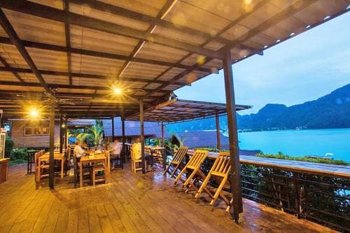 A cozy wooden deck restaurant overlooking a serene lake at dusk, featuring warm lighting and rustic furniture, ideal for travelers seeking a tranquil dining experience in nature.