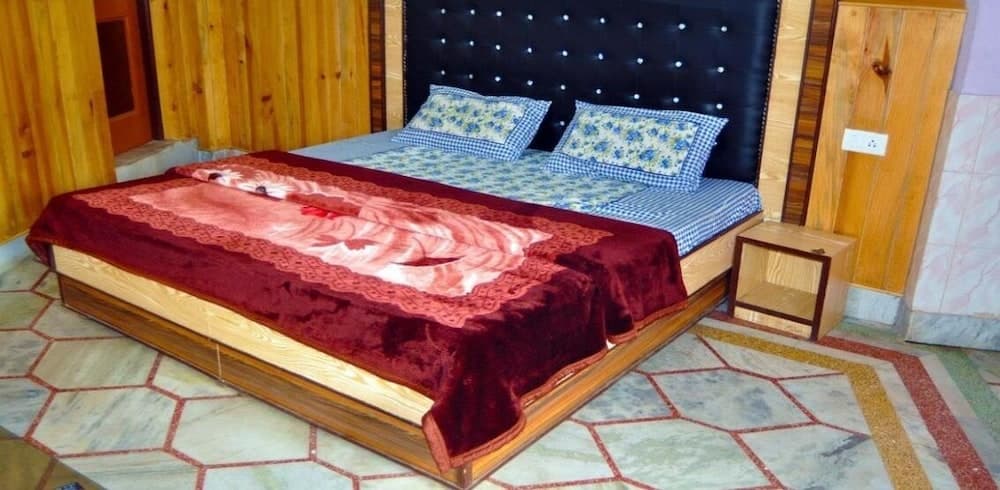A cozy bedroom with wooden walls, a plush bed adorned with floral pillows and a red blanket, and a tiled floor, ideal for travelers seeking comfort in a rustic retreat.