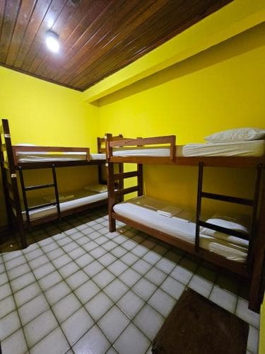 A cozy hostel room with vibrant yellow walls, wooden bunk beds, tiled flooring, and warm lighting creates an inviting atmosphere ideal for budget travelers seeking comfortable accommodations.