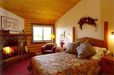 A cozy cabin bedroom with a warm fireplace, wooden walls, floral bedding, and festive wreath creates an inviting retreat perfect for a relaxing getaway.