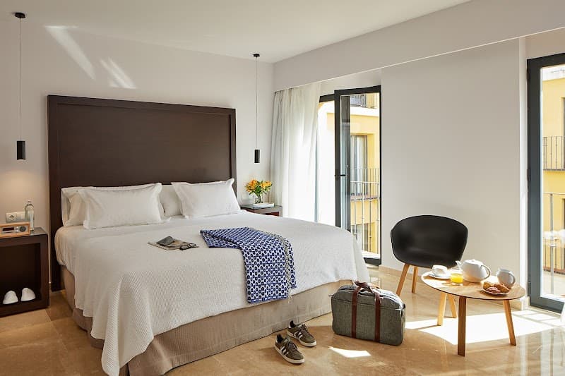 A cozy hotel room in Sevilla's historic center features a neatly made bed, modern furnishings, and a balcony view, ideal for travelers seeking comfort and charm during their Spanish getaway.