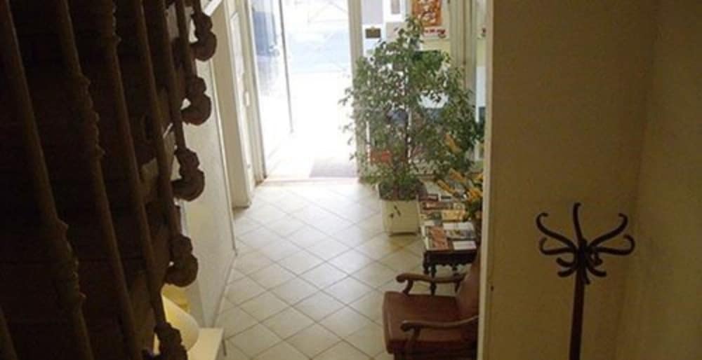 A cozy indoor hallway with tiled floors, ornate wooden staircase, potted plants, and a bookshelf creates a welcoming atmosphere ideal for travelers seeking a quaint and charming accommodation experience.