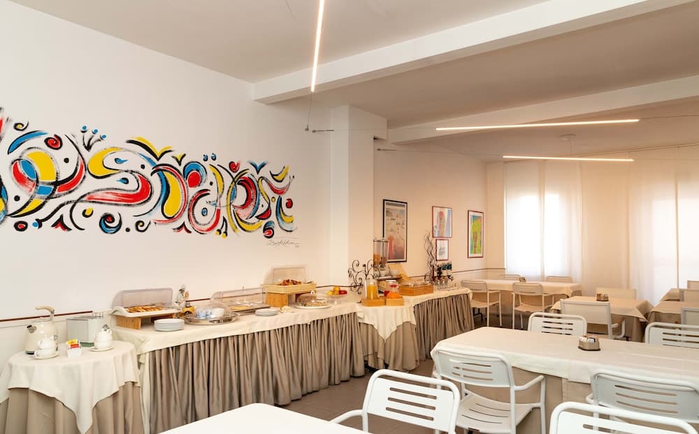 A cozy indoor dining area features vibrant wall art, neatly arranged tables with white chairs, and a buffet setup, ideal for travelers seeking a comfortable and artistic breakfast spot.