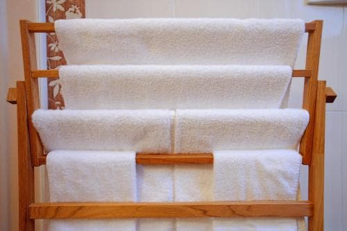 A neatly arranged wooden towel rack holding plush white towels in a clean bathroom setting evokes a sense of comfort and organization, ideal for travelers seeking cozy accommodations.