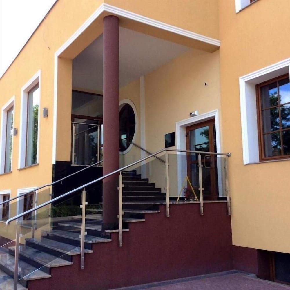 A welcoming yellow building entrance with a staircase, glass railing, and modern design invites travelers seeking accommodation or business services in a serene urban setting.