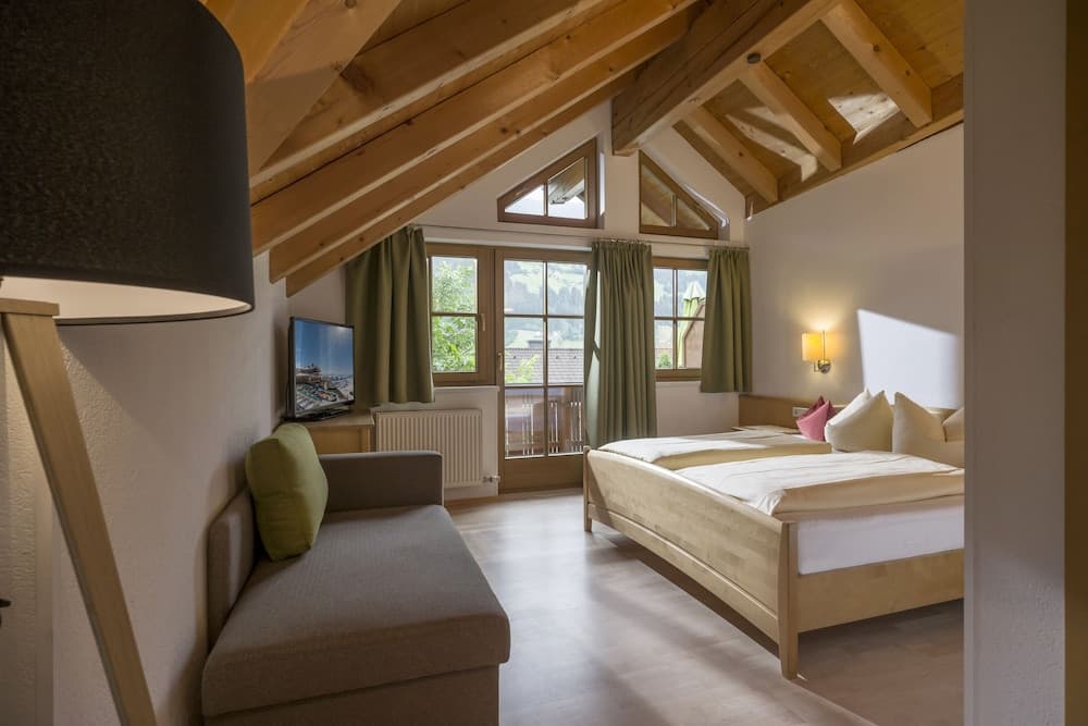 A cozy attic bedroom with wooden beams, large windows offering scenic views, and modern furnishings creates an inviting retreat ideal for travelers seeking relaxation in a charming lodge setting.