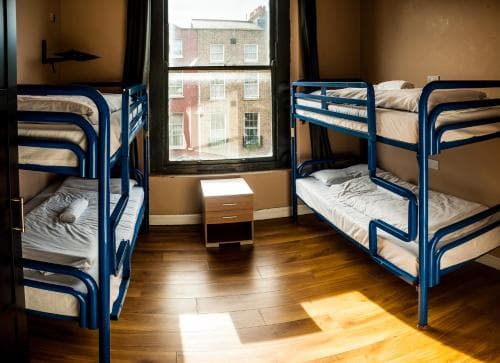 A cozy hostel room with blue bunk beds, wooden flooring, and natural light streaming through a window, ideal for budget travelers seeking a comfortable and communal stay.