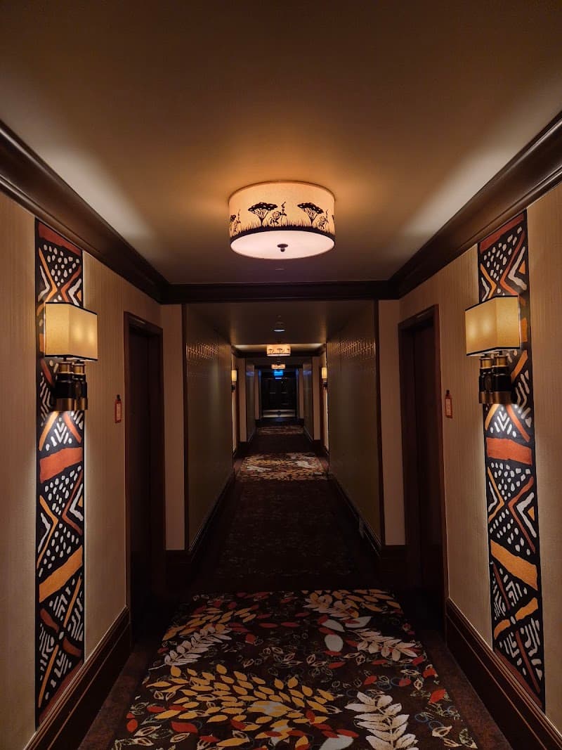 A warmly lit hotel corridor adorned with vibrant African-inspired artwork and patterned carpeting creates an inviting atmosphere at the Disney Explorers Lodge in Hong Kong, perfect for travelers seeking a themed adventure experience.