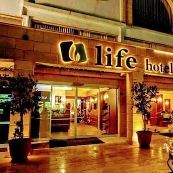 A warmly lit entrance to a modern hotel named "life hotel" features inviting glass doors, potted plants, and a cozy ambiance, ideal for travelers seeking comfort and style in an urban setting.