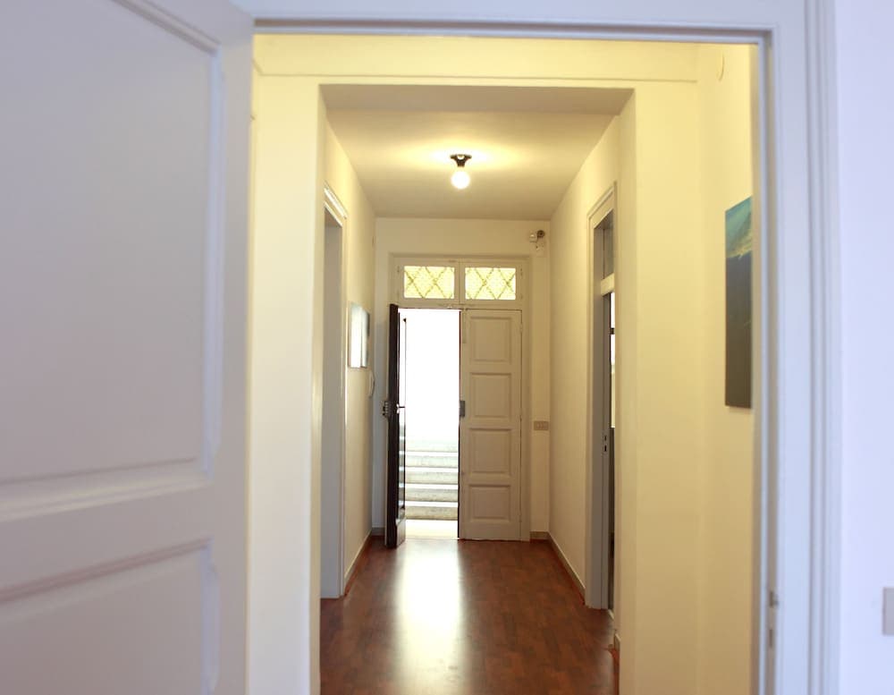 A warmly lit hallway with wooden floors, white walls, and a bright doorway at the end creates an inviting atmosphere, ideal for travelers seeking cozy accommodation interiors.